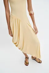 Vestido largo color amarillo pastel, confeccionado con mezcla de viscosa, con cuello redondo, manga corta y bajo asimétrico fruncido con volumen.