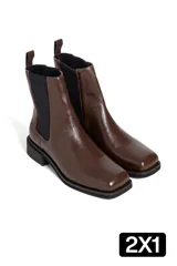 Botas tipo chelsea de cuero marrón con acabado brillante, paneles laterales elásticos negros y suela plana de goma negra.