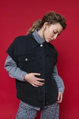 Chaleco de jean oversized color negro, con cuello camisero y cierre frontal con botones metálicos. Presenta un diseño estructurado con costuras reforzadas.