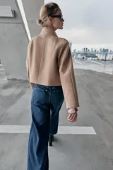 Chaqueta corta de paño en color beige, con cuello subido, manga larga y cierre frontal cruzado con botones oscuros. Presenta bolsillos delanteros de vivo.