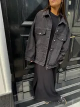 Campera clásica de jean negra con cuello camisero, bolsillos frontales y detalles de brillos plateados.