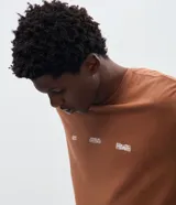 Remera de algodón color marrón con cuello redondo y mangas cortas. Presenta una estampa gráfica en la espalda con un diseño de paisaje montañoso y tipografía en color blanco.