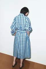 Trench largo de Zara con estampado de cuadros vichy en azul y blanco. Presenta cuello solapa, cierre frontal con botones, mangas largas y cinturón ajustable del mismo tejido. Incluye bolsillos de vivo en la parte delantera.