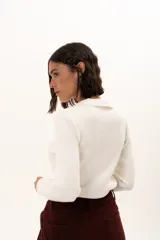 Sweater de tejido de punto fino color blanco, con cuello polo y escote en V, de manga larga y ajuste al cuerpo.