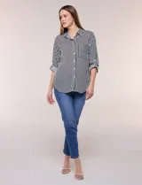 Camisa de corte clásico y silueta relajada con diseño de rayas verticales en blanco y negro. Presenta cuello camisero tradicional, cartera frontal con botones, un bolsillo aplicado en el pecho con rayas horizontales y mangas largas con sistema para arremangar.
