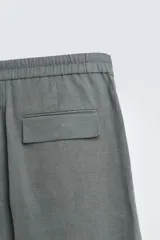 Pantalón de corte straight relaxed fit confeccionado en tejido de lino. Presenta cintura con pliegues frontales, cierre frontal con cremallera y botón, bolsillos laterales y bolsillos traseros con solapa.