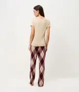 Pijama de dos piezas compuesto por una remera de manga corta en color beige con cuello redondo y un pantalón largo de corte recto con estampado de cuadros estilo argyle en tonos bordó y beige, con cintura elástica.