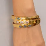 Brazalete rígido dorado con tres piedras incrustadas: una labradorita ovalada en el centro y dos piedras de la luna redondas a los lados.