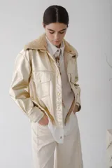 Camisa de cuero metalizado color champagne, con cuello de piel sintética color beige, cierre frontal con botones dorados, bolsillos con solapa en el pecho y corte recto.