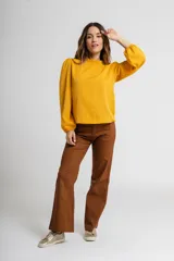 Blusa color mostaza con cuello alto fruncido y mangas largas abullonadas con puños elásticos.