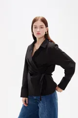 Camisa blanca de algodón con diseño cruzado y anudado lateral, cuello camisero y mangas largas con puños.