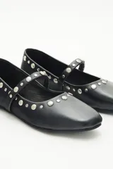 Balerinas negras de cuero con tira sobre el empeine y remaches de níquel de distintos tamaños.