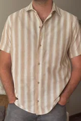 Camisa de manga corta con estampado a rayas verticales color beige y blanco, con cuello clásico y cierre abotonado.