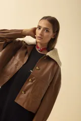 Campera de cuero color suela con cuello de corderito sintético en tono crema. Presenta cierre frontal con botones grandes de carey y bolsillos frontales tipo parche.