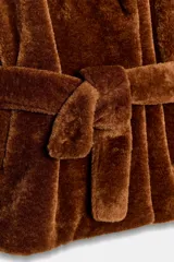 Chaqueta de textura efecto pelo en color marrón, con cuello de solapa, manga larga y cierre frontal cruzado mediante un cinturón del mismo tejido. Cuenta con bolsillos delanteros.
