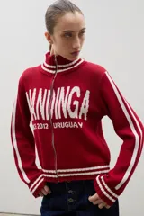 Campera tejida de punto color marrón con cierre frontal completo, cuello alto y detalles de rayas blancas en cuello, puños y ruedo. Presenta el logo de la marca estampado en el frente.