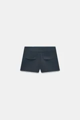 Shorts de tiro medio en color crudo, con bolsillos laterales delanteros y cierre frontal con cremallera y ganchos metálicos.
