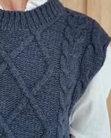 Chaleco de punto gris oscuro con diseño de trenzas y rombos en relieve, cuello redondo y terminaciones acanaladas.