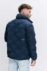 Cazadora acolchada de color azul marino con diseño de costuras onduladas, cierre frontal con cremallera y cuello alto. Presenta bolsillos frontales y un ajuste cómodo.