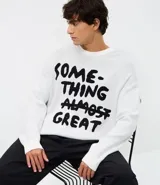 Suéter de corte boxy confeccionado en tejido jacquard de viscosa y poliéster. Presenta cuello redondo, mangas largas y un diseño estampado con lettering en color negro sobre fondo blanco.