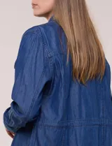Sobrecamisa azul de denim de algodón liviano, con cuello camisero, cierre frontal de botones, bolsillos con solapa en el pecho y cordón ajustable en la cintura.