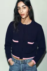 Chaqueta de punto de cuello redondo y manga larga, con cierre frontal de botones. Presenta dos bolsillos delanteros de plastrón y detalles de ribetes en color rosa a contraste en los puños, el ruedo y los bolsillos.