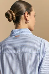 Camisa azul a rayas blancas, de manga larga con puños elastizados, entallada en la cintura y con cierre de botones frontales.