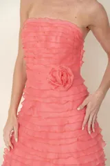 Vestido corto de organza color salmón, strapless, con volados horizontales en el torso y falda, y flor de la misma tela en la cintura.
