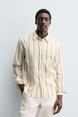Camisa de corte relajado confeccionada en tejido mezcla de algodón, con diseño de rayas verticales, cuello solapa, manga larga con puños abotonados y cierre frontal de botones.