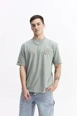 Remera de manga corta color verde salvia, con cuello redondo y un estampado gráfico en la espalda que incluye tipografía en rojo y blanco, y fotografías en blanco y negro.