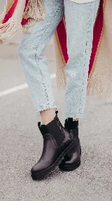 Bota tipo Chelsea de cuero negro con paneles elásticos laterales y suela track dentada. Presenta un diseño minimalista con tirador en la parte trasera.