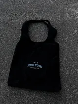 Bolso tote negro con asas cortas y estampado frontal con la inscripción "1989 New York Manhattan" en color blanco.