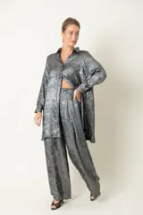 Camisa plateada de poliéster con textura metalizada, corte amplio, cuello clásico, cierre frontal con botones y mangas largas con puños abotonados.