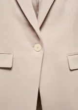 Blazer entallado de color beige con solapas de muesca, hombros estructurados y cierre frontal de un botón. Presenta bolsillos de ribete delanteros, pinzas de entalle y abertura posterior.