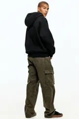 Campera negra con capucha, cierre frontal y bolsillo canguro dividido. Presenta un corte oversized con hombros caídos y puños y bajo acanalados.