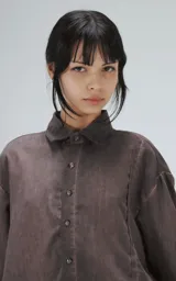 Camisa de corte oversize y mangas cortas, confeccionada en tela con efecto de teñido artesanal maltinto en tono gris. Presenta cuello clásico, cierre frontal con botones y costuras verticales decorativas en el frente.