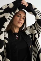 Saco tipo cardigan de punto, color negro con diseño de notas musicales y compases en color crema. Presenta cierre frontal con botones, cuello en V y puños acanalados.