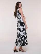 Vestido maxi sin mangas de seda fría, color negro con estampado floral blanco y verde. Presenta escote cruzado con detalle de abertura y corte en la cintura con falda amplia.