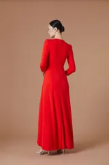 Vestido largo negro de corte elegante con escote en V y mangas tres cuartos. Presenta detalles de pedrería brillante en el borde del escote y en los puños, con un diseño drapeado en la cintura que aporta movimiento y realza la silueta.