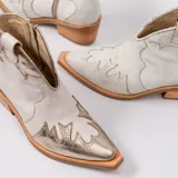 Botín de cuero vacuno color marrón oscuro, con taco de madera foliado en cuero de 5cm de altura, cierre lateral interno y horma de punta fina.