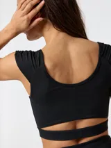 Crop top deportivo negro con fruncido frontal en el pecho, tirantes anchos y aberturas inferiores que dejan al descubierto la zona bajo el busto, confeccionado con tecnología Aloe Vera.