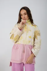 Buzo oversize color crema con estampado de hojas en tonos verde y amarillo, cuello alto con medio cierre metálico y jareta en la cintura para ajustar.