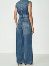 Enterito de jean azul con corte amplio, cuello camisero, sin mangas, con bolsillos delanteros y cierre frontal con botones.