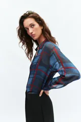 Camisa de manga larga con cuello solapa y cierre frontal con botones. Presenta un diseño de cuadros en tonos azules y rojos sobre un tejido semitransparente.