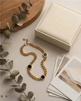 Collar de cadena tipo eslabón grueso con baño de oro, que presenta tres dijes circulares con piedra ónix negra y detalles de números romanos en los bordes.