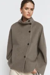 Cazadora de corte amplio confeccionada en hilatura con lana, color beige. Presenta cuello subido, manga larga y cierre frontal con botones negros. Destaca por sus acabados con costuras de hilo a contraste en los bordes.
