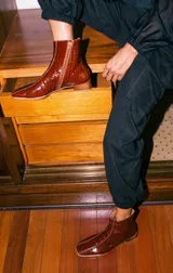 Botinetas de cuero con textura croco acharolado en color negro. Presentan un diseño de punta cuadrada, cierre lateral y un taco bajo de madera.