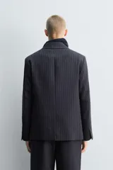 Blazer de corte relajado confeccionado en tejido de lana con estampado de raya diplomática. Presenta cuello con solapas de muesca, cierre frontal de dos botones, bolsillos de vivo en la cadera y abertura central en la espalda. Incluye forro interior a contraste.