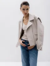 Chaqueta corta estilo biker color beige, confeccionada en piel sintética. Presenta cierre asimétrico frontal, bolsillo con cierre a la vista y bolsillo con solapa, cinturón con hebilla en la cintura.