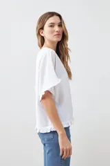 Blusa blanca de corte holgado con cuello redondo, mangas cortas con detalle de volados y ruedo con terminación de volado pequeño.